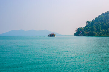 Beautiful tropical landscape. A ship sails across the blue sea, mountains overgrown with vegetation on the coast