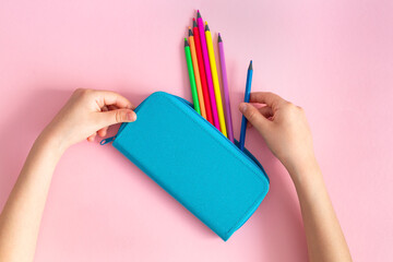 Rainbow multicolored pencils in a blue pencil case in the hands of a child on a pink background. Stationery, school supplies. Concept back to school, preschool education. Mockup, copy space. - obrazy, fototapety, plakaty