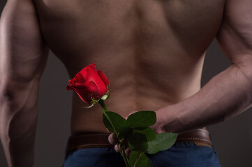Athletic man holding a red rose behind his back