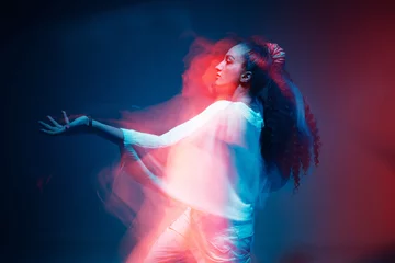 Poster Colourful portrait of young mixed race girl dancing in studio. Long exposure. Colored neon light. © Georgii