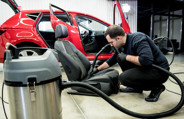 Car service worker cleaning car seat with vacuum cleaner.