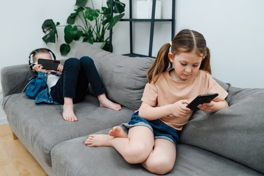 Busy little siblings spending their free time watching their phones on a couch, playing or watching cartoons. In the living room.