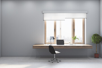 Bright grey room with a wooden desk and computer, big window and concrete floor and walls, interior design and workspace concept, 3d rendering, mock up