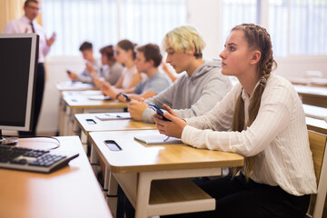 Group of modern teenagers sitting with mobile phones on lesson in classroom