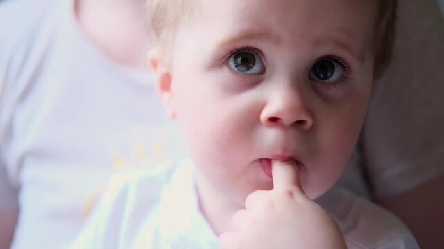 4K cute little baby boy sucking thumb sitting in mom's hands
