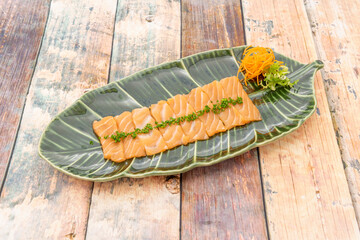 Raw salmon slices with chopped chives and carrot shavings on a green leaf shaped plate
