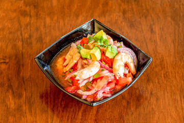 Ceviche in a black bowl with a generous serving of prawns, tomato, avocado, parsley