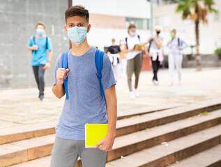 Teenager in a protective mask walking in the street, carrying a bag on one shoulder