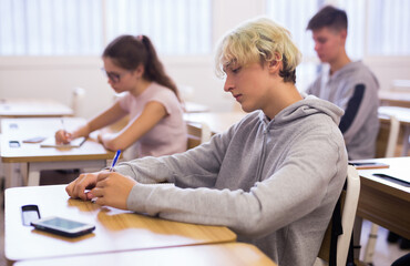 Obraz premium Diligent teenage high school student studying in college with classmates, making notes of teacher lecture..