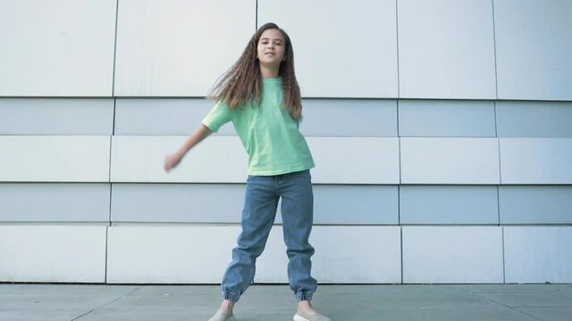 Caucasian beautiful girl 8-10 years old. The child is dancing a modern pop dance and smiling. Gorgeous curly hair.