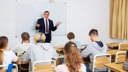 Man teacher with notebook is giving interesting lecture for students in the classroom