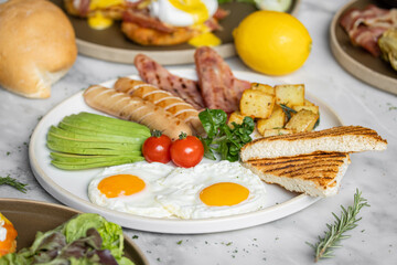 Fototapeta na wymiar English breakfast menu with fried eggs,ham,avocado-slices ,deep fried potatoes,sausage and tomato
