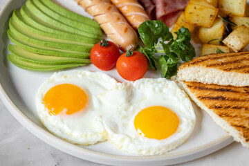 English breakfast menu with fried eggs,ham,avocado-slices ,deep fried potatoes,sausage and tomato