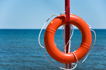 Marine life buoy life saving orange swimming ring on a beach with blue sea in the background