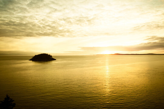 A Beautiful Yellow Sunset Over The Ocean With An Island And Mountains In The Distance.