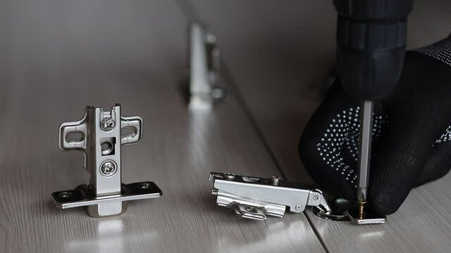 Installing a furniture hinge on the door. Assembling furniture and fixing fittings close-up. Screwing the door hinge onto a piece of furniture with a screwdriver.