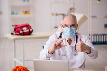 Old male doctor working in the clinic during pandemic