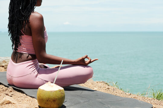 Cropped image of fit strong young woman meditating on rock and looking at beautiful seascape