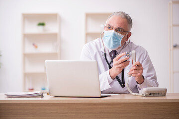 Old male doctor working in the clinic during pandemic