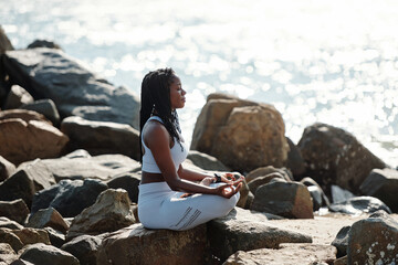 Calm relaxed sportswoman sitting on rocky beach, enjoying sea breeze and meditating