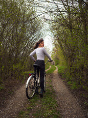 Fototapeta premium A woman with a bicycle on a country road under flowering trees.