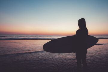 Silhouette of beautiful sexy surfer female with surfboard on the sandy beach at sunset. water...
