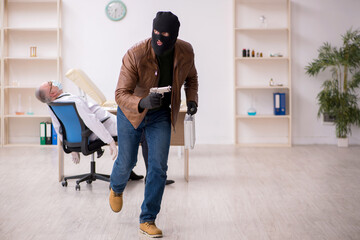 Masked man burglar stealing vaccine from old doctor