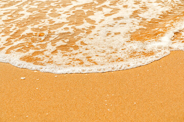 A sea wave with white foam splashes out onto the yellow sandy shore