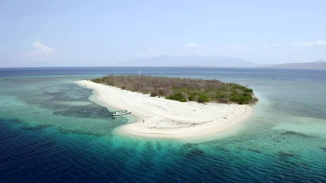 Aerial Rising Above A Boat On The Beach Of A Small Coral Reef Island Surrounded By Shimmering Deep Blue Ocean Extending To The Horizon - East Java, Indonesia
