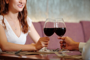 Close-up image of young couple toasting with glasses of red wine when sitting at restaurant table