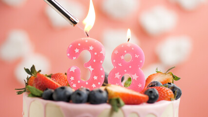 Birthday cake number 38, pink candle on beautiful cake with berries and lighter with fire against...