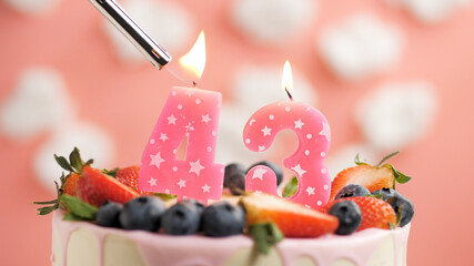 Birthday cake number 43, pink candle on beautiful cake with berries and lighter with fire against background of white clouds and pink sky. Close-up - obrazy, fototapety, plakaty