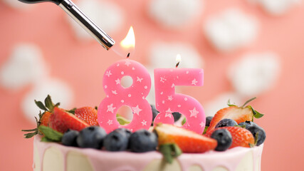 Birthday cake number 85, pink candle on beautiful cake with berries and lighter with fire against...