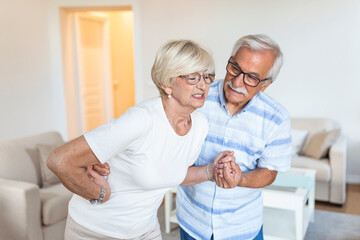 Fototapeta premium Senior couple at home. Handsome old woman is having back pain and her attractive old husband supports her.