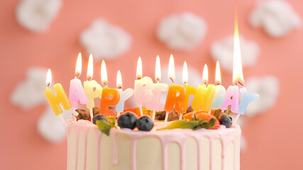 Birthday cake with candle title Happy Birthday on beautiful cake with berries background of white clouds and pink sky. Close-up