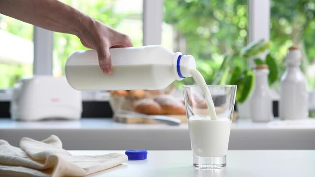 Pouring milk from plastic bottle into a glass in the kitchen