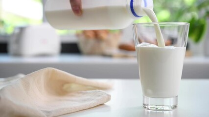 Pouring milk from plastic bottle into a glass in the kitchen