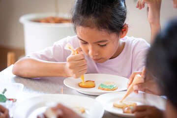 Close up asian child girl squeezing icing cream to decorate cookies with friend with fun. DIY homemade kid art and craft concept.