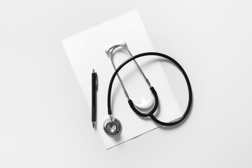 Modern stethoscope, sheet of paper and pen on light background