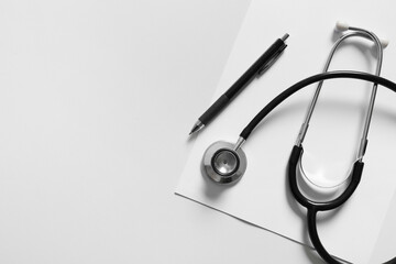 Modern stethoscope, sheet of paper and pen on light background