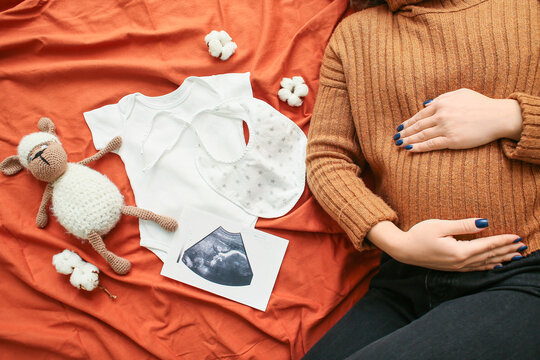 Pregnant Woman With Sonogram Image And Baby Accessories On Bed