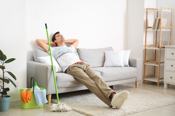 Young man with cleaning supplies relaxing in living room