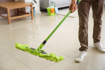 Young man mopping floor in living room