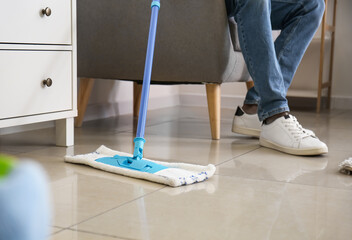 Young man with floor mop in living room, closeup