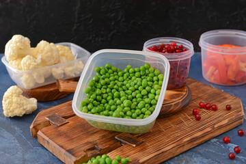 Plastic containers with vegetables on table against dark background