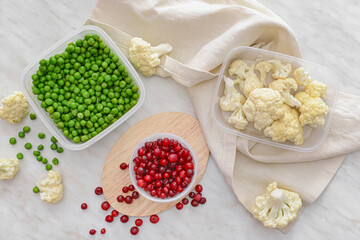 Plastic containers with vegetables and cranberry on light background