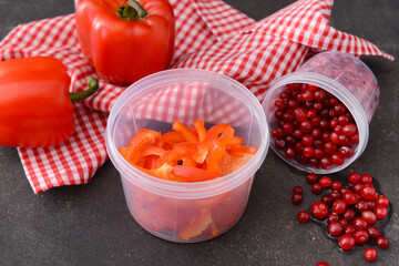 Plastic containers with bell peppers and cranberry on dark background, closeup