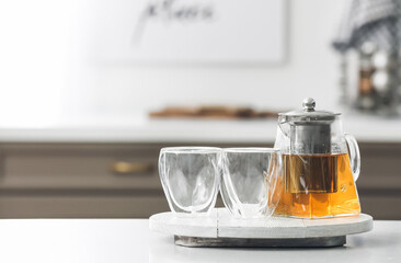 Teapot with hot tea and glasses on table in kitchen