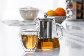 Teapot and glass with hot tea on table in kitchen