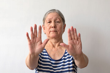 An elderly woman, a gray-haired lady of the 60s in a striped white and blue dress, doing stop gesture with hands palms, angry and frustration expression.